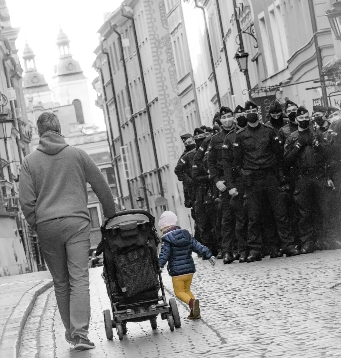 Adult pushing a stroller while a small child walks toward a line of police officers